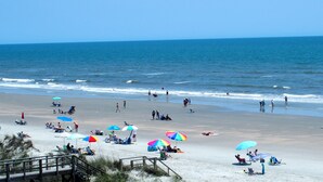 A beach with people sunbathing and swimming, and a wooden boardwalk leading to the water. - Oceanfront Heaven in Exclusive West End, Ocean Isle Beach, NC  (Ocean Isle Beach)