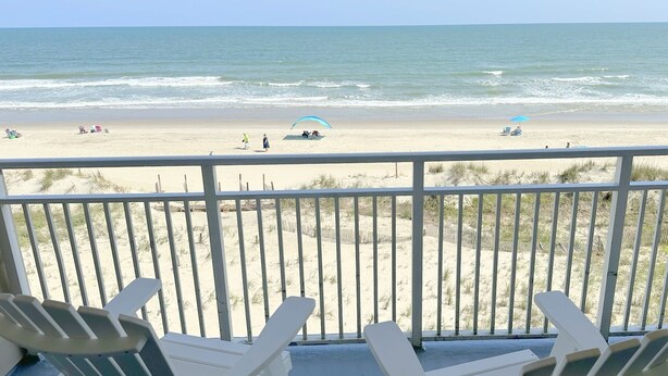 A balcony with white Adirondack chairs overlooking a beach with a sandy shore and ocean waves. - Oceanfront Heaven in Exclusive West End, Ocean Isle Beach, NC  (Ocean Isle Beach)