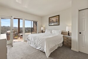 Relax in this serene retreat with a large bed, bedside tables, and a balcony overlooking a forested area.