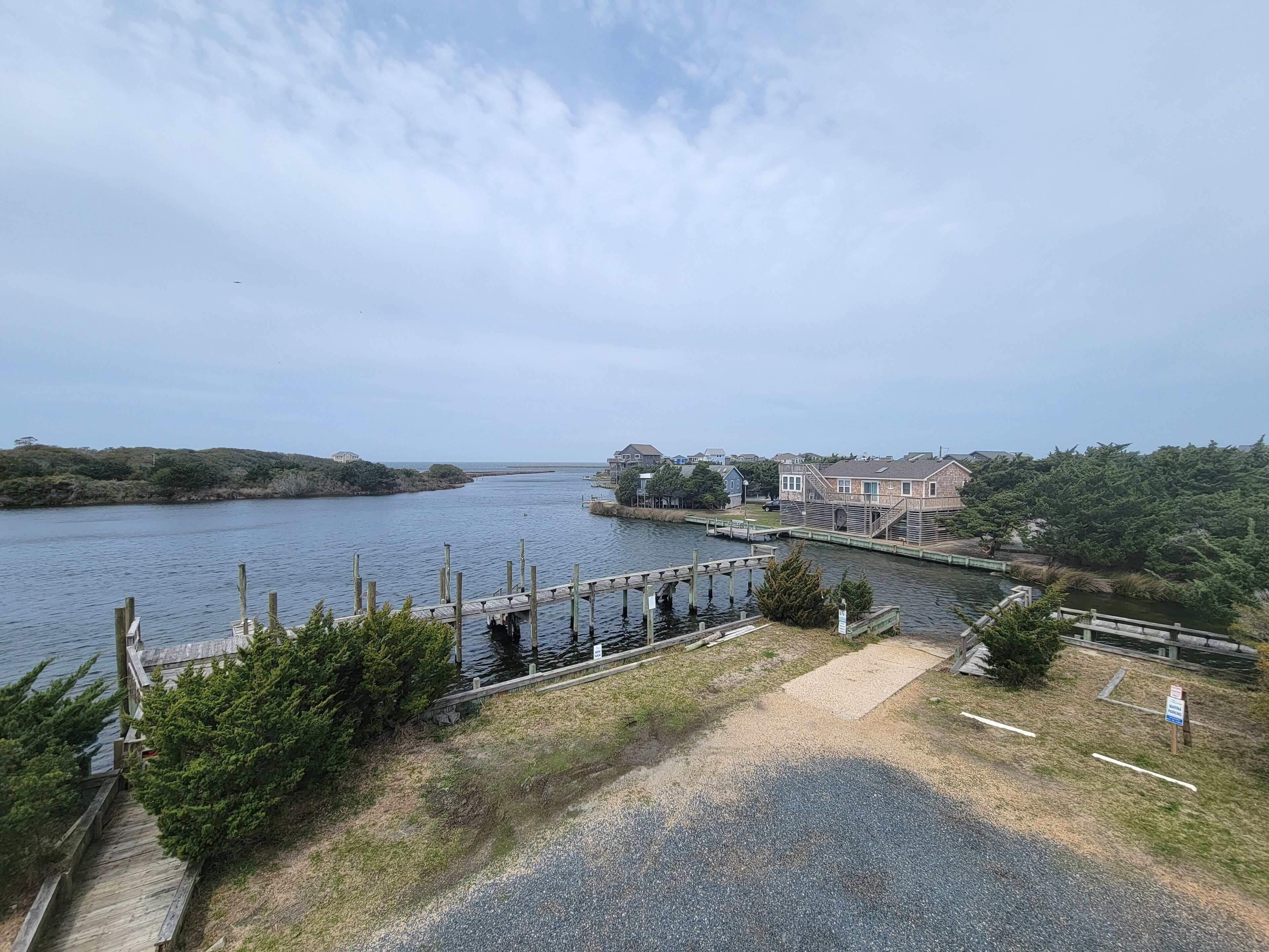 A waterfront property with a dock, a wooden staircase, and a grassy area leading to a building with a large window overlooking the water.
