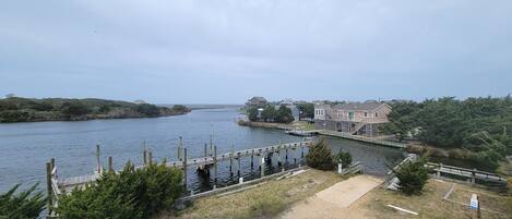 A waterfront property with a dock, a wooden staircase, and a grassy area leading to a building with a large window overlooking the water.