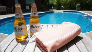 Two bottles of Modelo beer and a folded towel on a wooden table by a swimming pool. - Secluded Getaway: Bear Mt, Cold Spring, Beacon, West Point!   (Garrison)