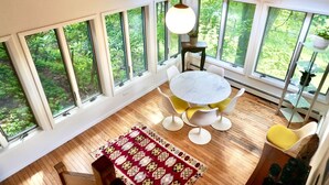 A room with a round table and chairs, large windows, and a hanging light fixture. - Secluded Getaway: Bear Mt, Cold Spring, Beacon, West Point!   (Garrison)