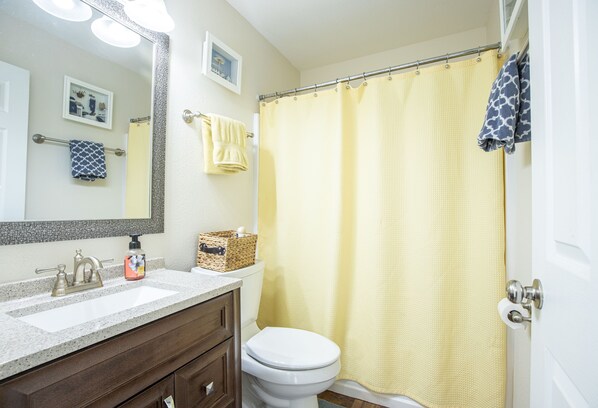 Un baño con inodoro blanco, lavabo color beige y cortina de ducha amarilla.