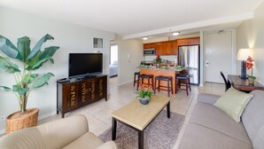 A modern living room with a sofa, a coffee table, a TV, and a kitchen area with a refrigerator, microwave, and bar stools. - Amazing views of Diamond Head, Waikiki Beach, and the Pacific Ocean! (Honolulu)