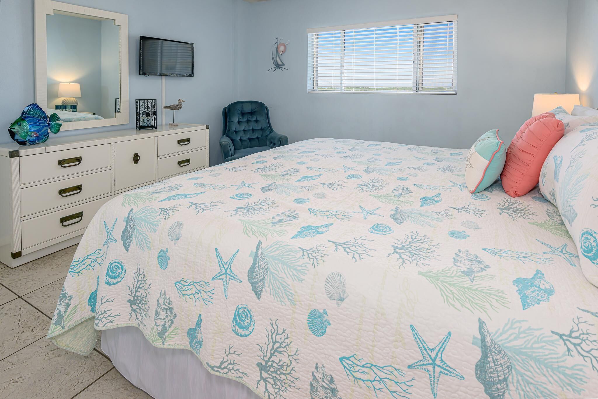 Un dormitorio con cama, cómoda, silla y televisor en la pared.