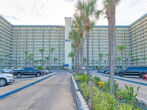 A large hotel with multiple floors, a parking lot, and palm trees.