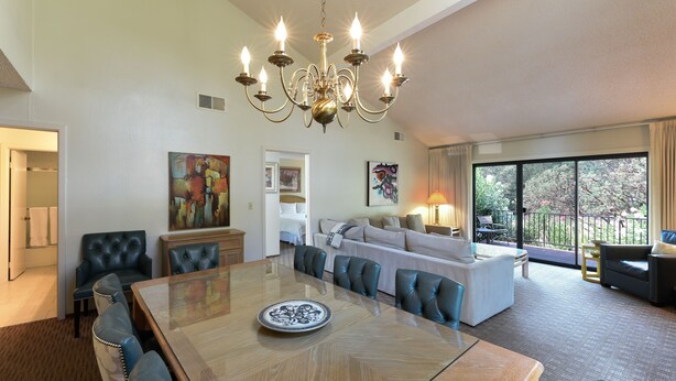 A spacious living area with a large dining table, comfortable seating, a chandelier, and a balcony with a view.