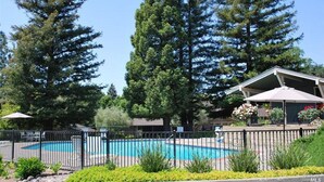 A swimming pool surrounded by a fence, with tall trees in the background and a building with an umbrella.