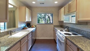 A kitchen with granite countertops, a double sink, a stove, and a window with a view of trees.