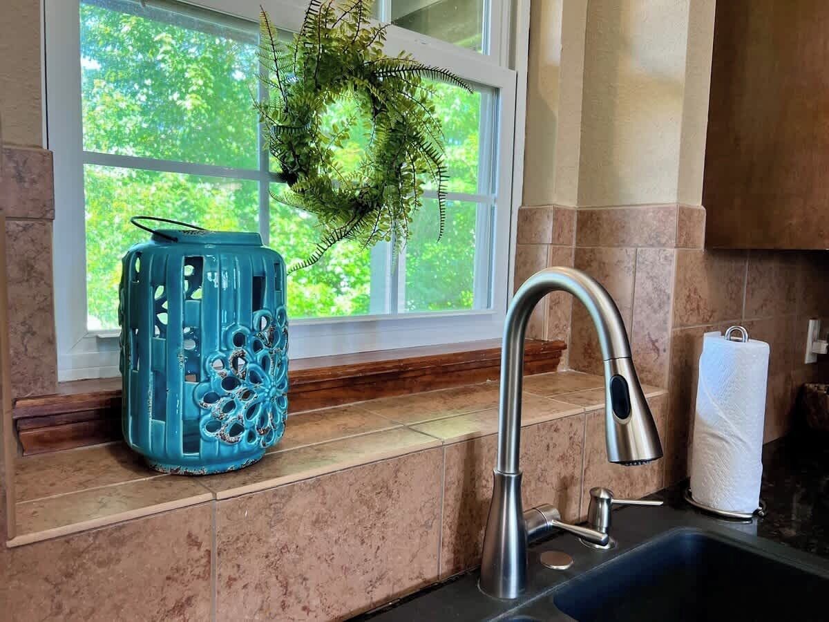 Eine Küche mit einem Edelstahlarmaturen, einem blauen Dekoelement und einem Fenster mit Blick auf Grünflächen.
