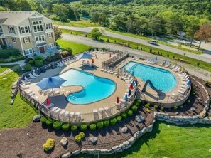 A large outdoor swimming pool with a slide, surrounded by lounge chairs and umbrellas, and a building in the background. - The Great Escape/Pools/Table Rock Lake (Hollister)