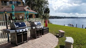 Un patio exterior con dos parrillas de barbacoa, una mesa de piedra y vistas a un lago.