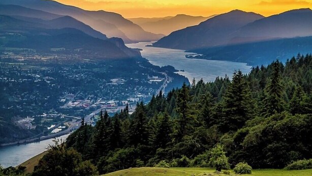 Un paysage montagneux avec une rivière, une forêt dense et une ville.