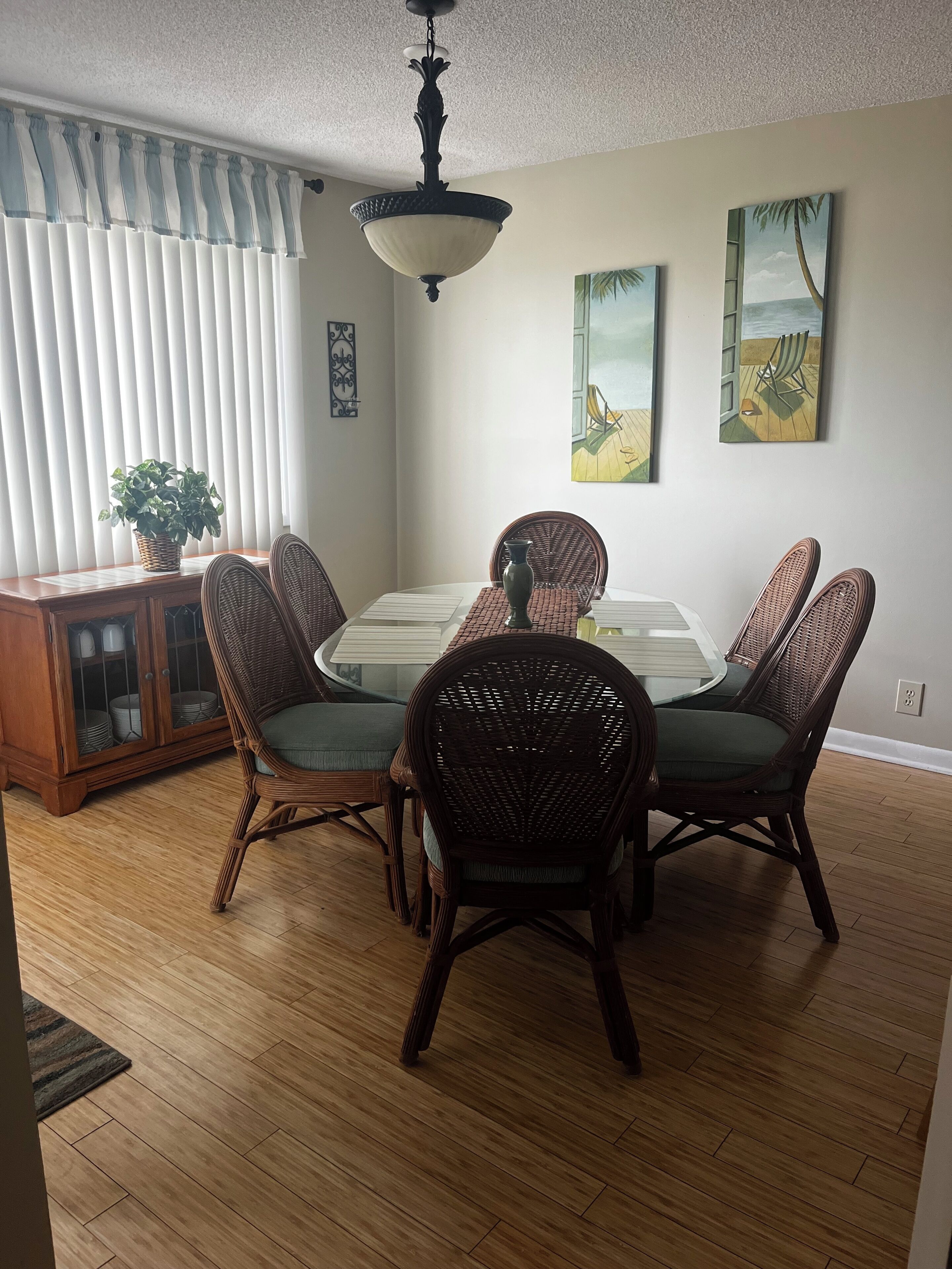 A dining area with a table, wicker chairs, a wooden cabinet, and artwork on the walls.