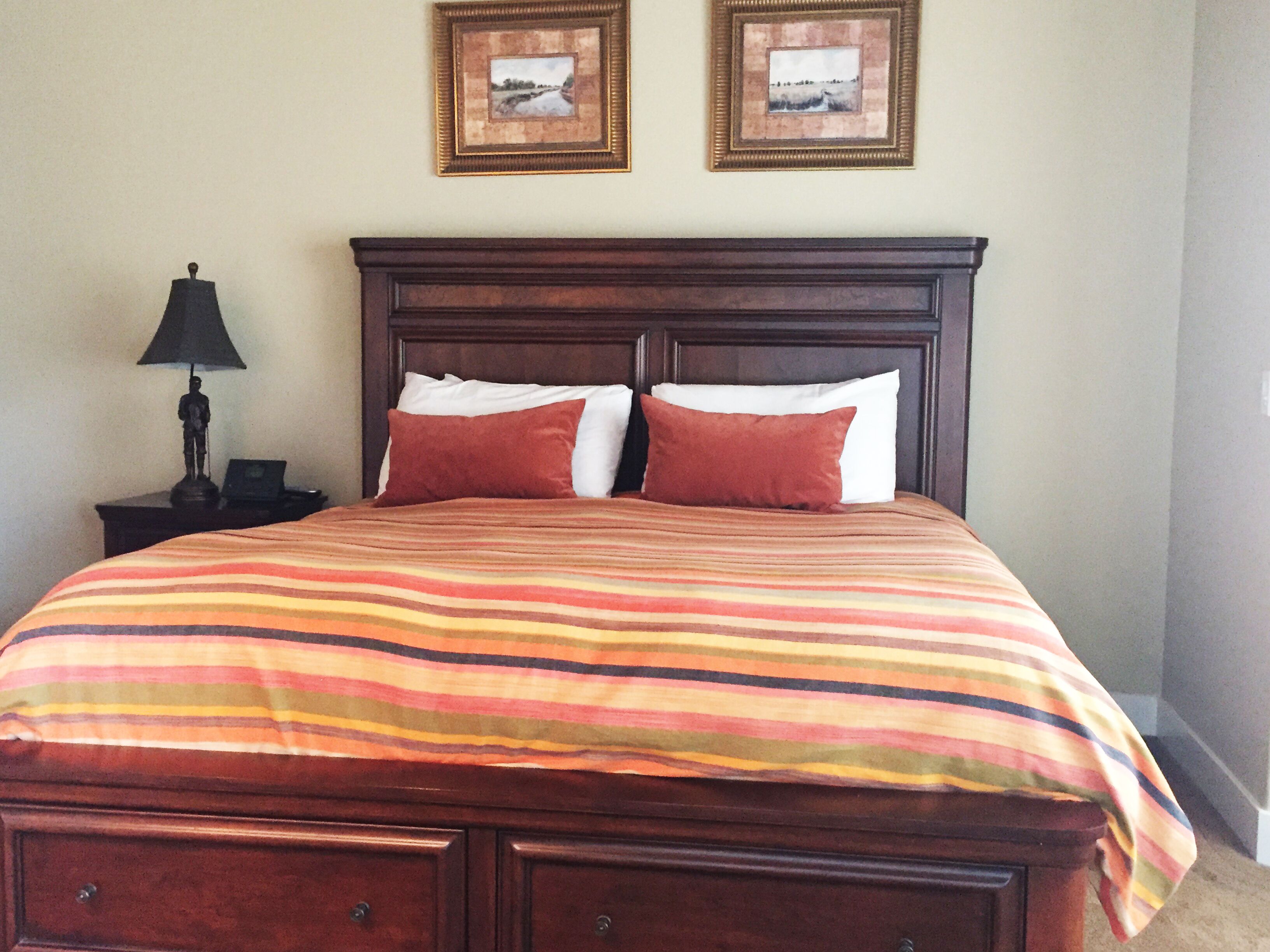 A bed with a striped bedspread, two pillows, a nightstand with a lamp, and two framed pictures on the wall.
