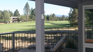 Um deck coberto com cadeiras de lounge, com vista para um campo de golfe e uma casa ao fundo.