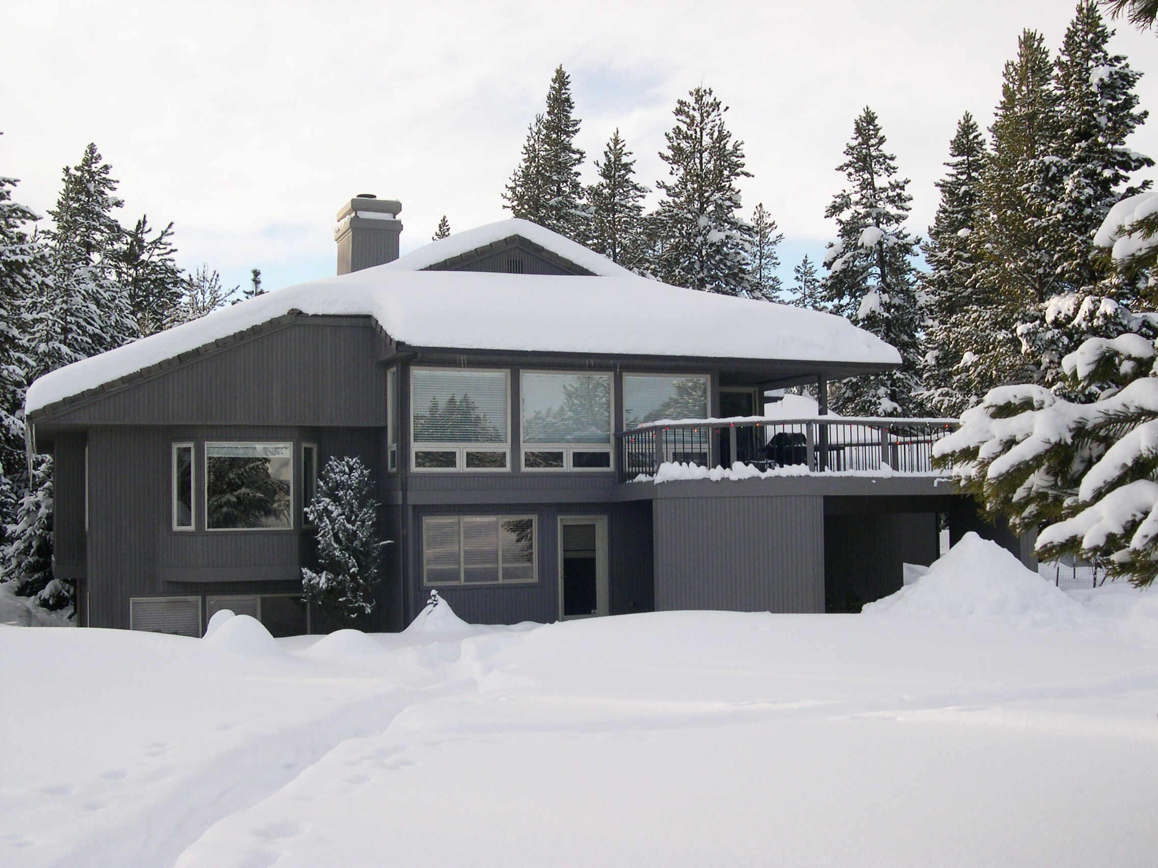 Ein modernes, zweistöckiges Haus mit Balkon, umgeben von schneebedeckten Bäumen.
