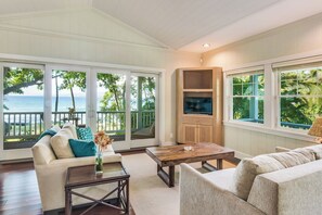 A spacious living room with a large window overlooking the ocean, a cozy seating area, and a wooden coffee table. - Luxurious Oceanfront Beach House w/AC & Stunning Coastal Views: Puako Bay (74) (Kamuela)