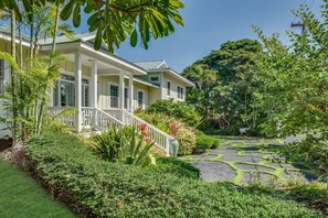 A two-story house with a covered porch, surrounded by lush greenery and a garden with patterned grass. - Luxurious Oceanfront Beach House w/AC & Stunning Coastal Views: Puako Bay (74) (Kamuela)