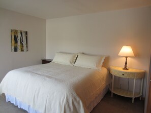 A neatly made bed with a white duvet, a bedside lamp, and a small bedside table with a patterned tray. - Waterfront Pearl Home Away from Home (Portland)