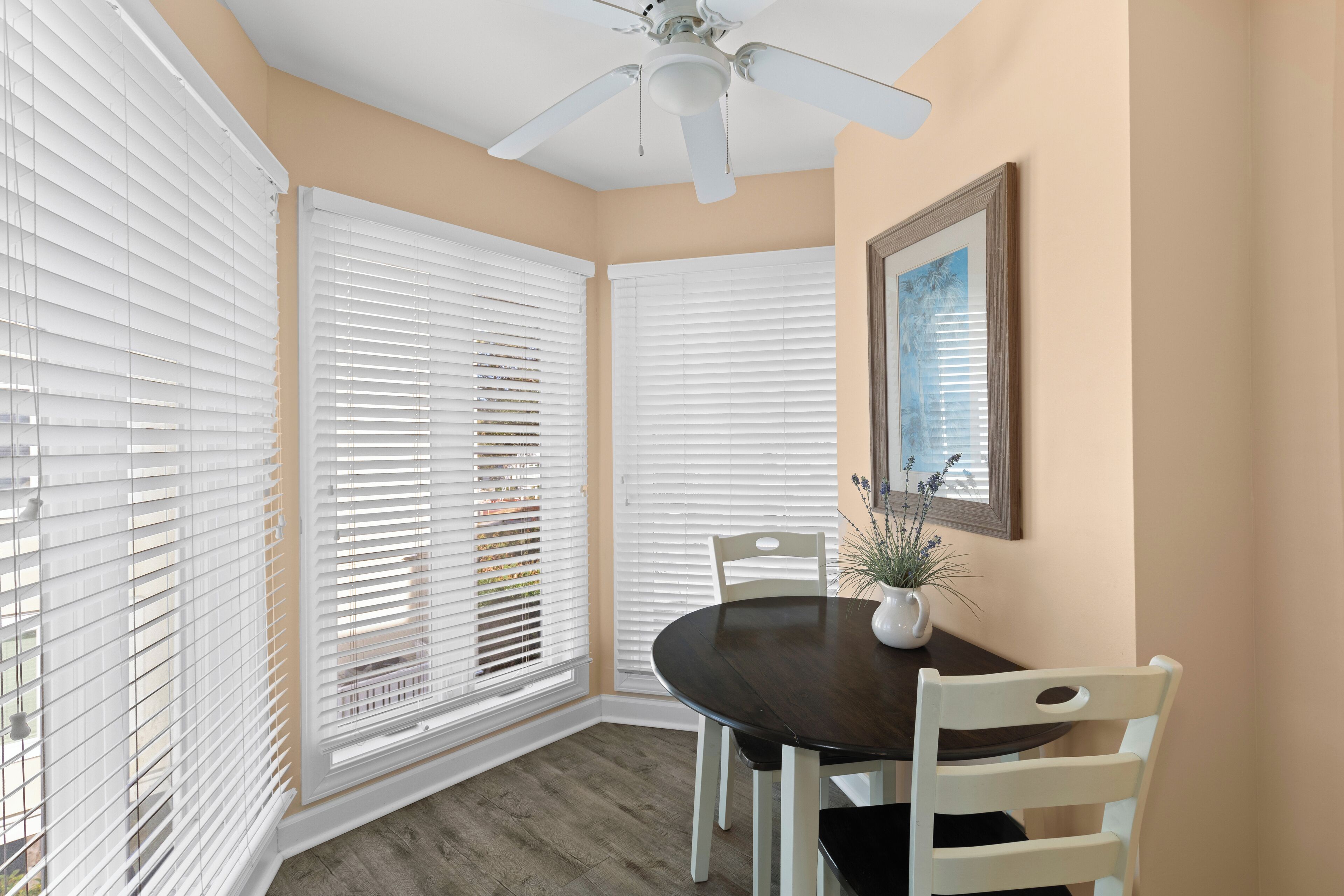 A dining area with a dark wooden table, white chairs, and a ceiling fan.