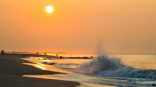 A beach scene with the sun setting over the ocean, waves crashing onto the shore, and a lifeguard tower in the distance. - Short walk to the Beach, sleeps 8, four bedrooms, private patio, 2026 weeks open (Cape May)