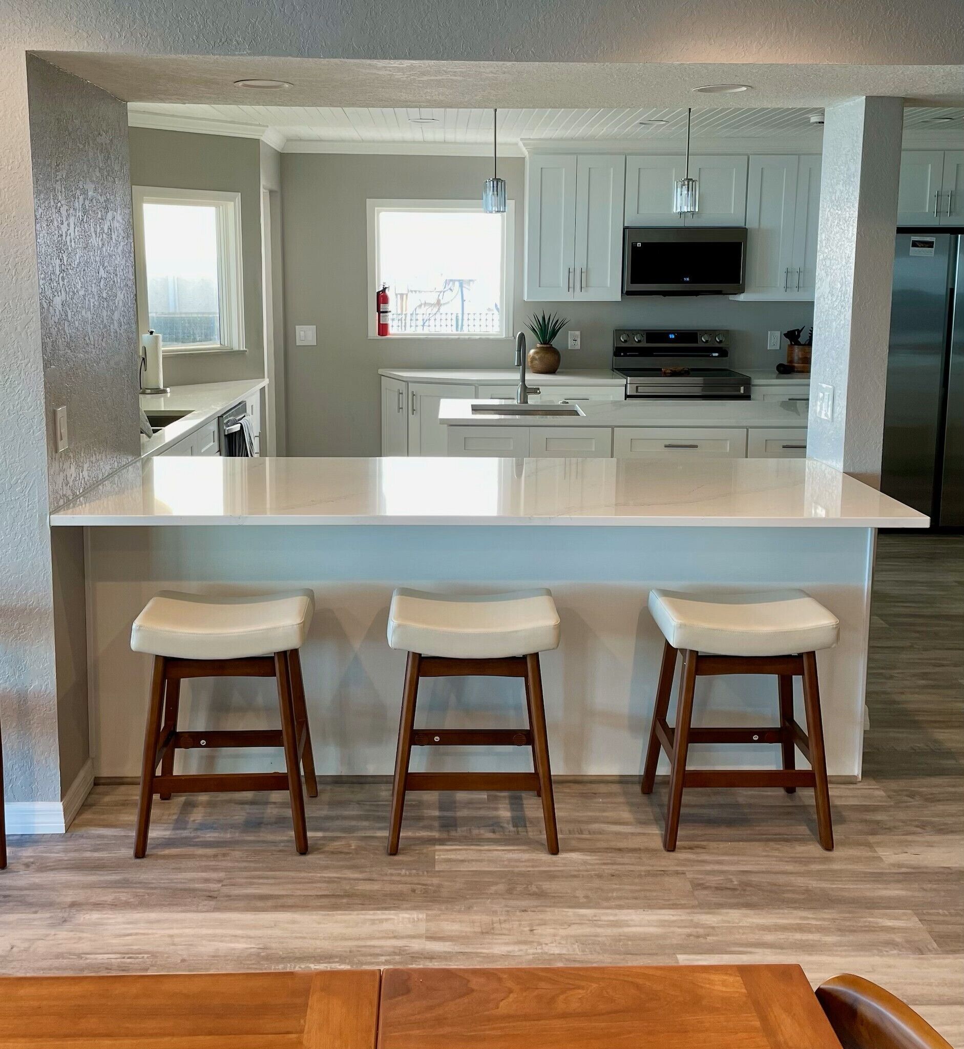 Una cocina moderna con una isla grande, armarios blancos y tres taburetes de madera.