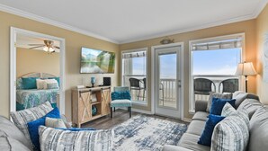 A living room with a sofa, chairs, a coffee table, a TV, a ceiling fan, and a view through the glass doors. - "Beachfront Paradise - Wake Up to Ocean Views & Waves! (Galveston)