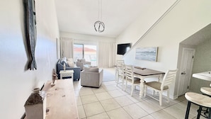 Ett modernt vardagsrum med en soffa, ett matbord och stolar. Det finns en tv monterad på väggen och ett fönster med gardiner.