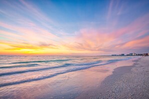Ein Strand mit Sonnenuntergang, Wellen und Gebäuden in der Ferne.