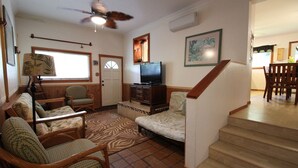 A living room with a sofa, chairs, a television, a staircase, and a dining area.