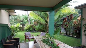 A covered patio with a table and chairs, surrounded by lush tropical plants and a well-maintained lawn.
