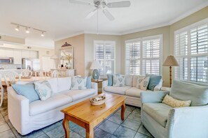 A spacious living room with a white sofa set, a wooden coffee table, and a dining area with white chairs.