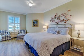 A bedroom with a bed, two matching chairs, a nightstand with a lamp, a wall-mounted branch decoration, and a window with blinds.