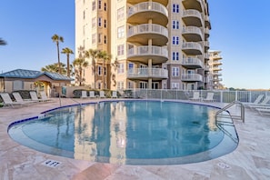 A swimming pool with a 4 ft depth marker, surrounded by lounge chairs and a multi-story building with balconies.