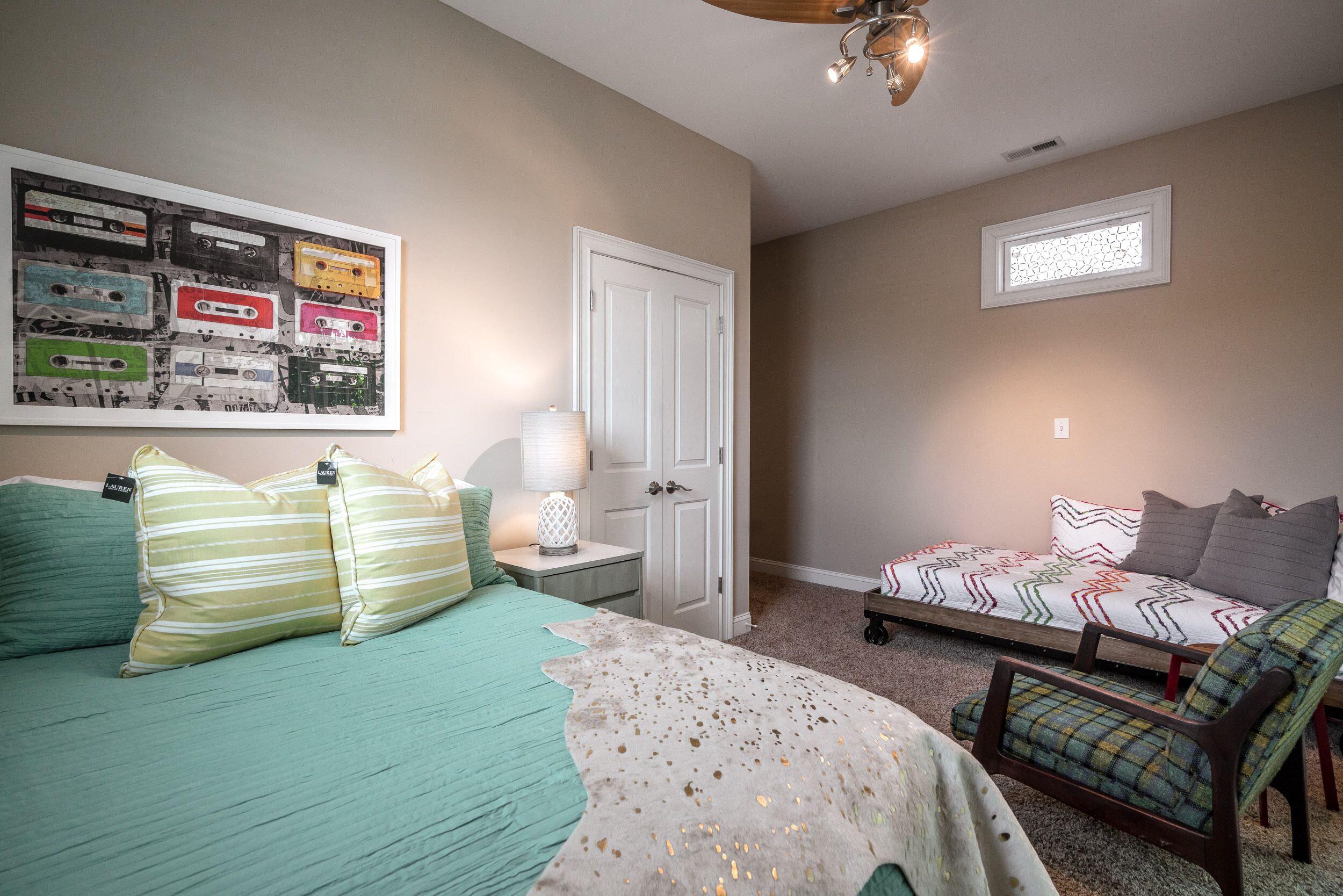 A bedroom with a bed, a chair, a sofa, a door, and a wall with a poster.