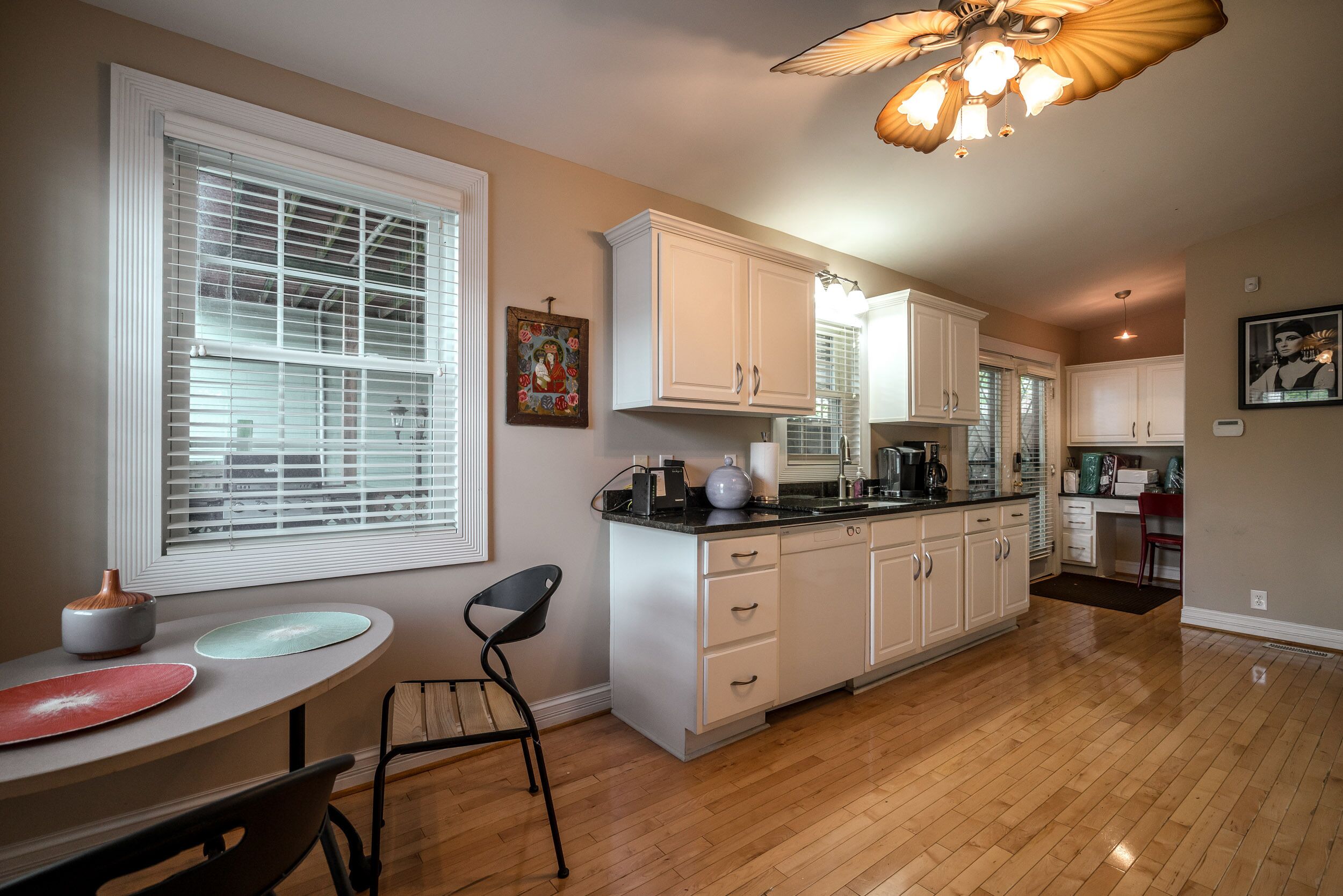 A modern kitchen with white cabinets, a dining table with chairs, and a large window with blinds.