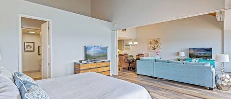 A spacious bedroom with a large bed, a dresser, and a television in the living area.