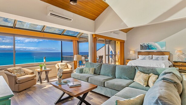 A spacious living room with a large sofa, a coffee table, and a view of the ocean through large windows.