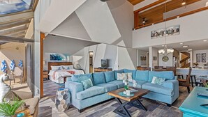 A spacious living area with a large blue sofa, a wooden coffee table, and a dining area with a kitchen in the background.