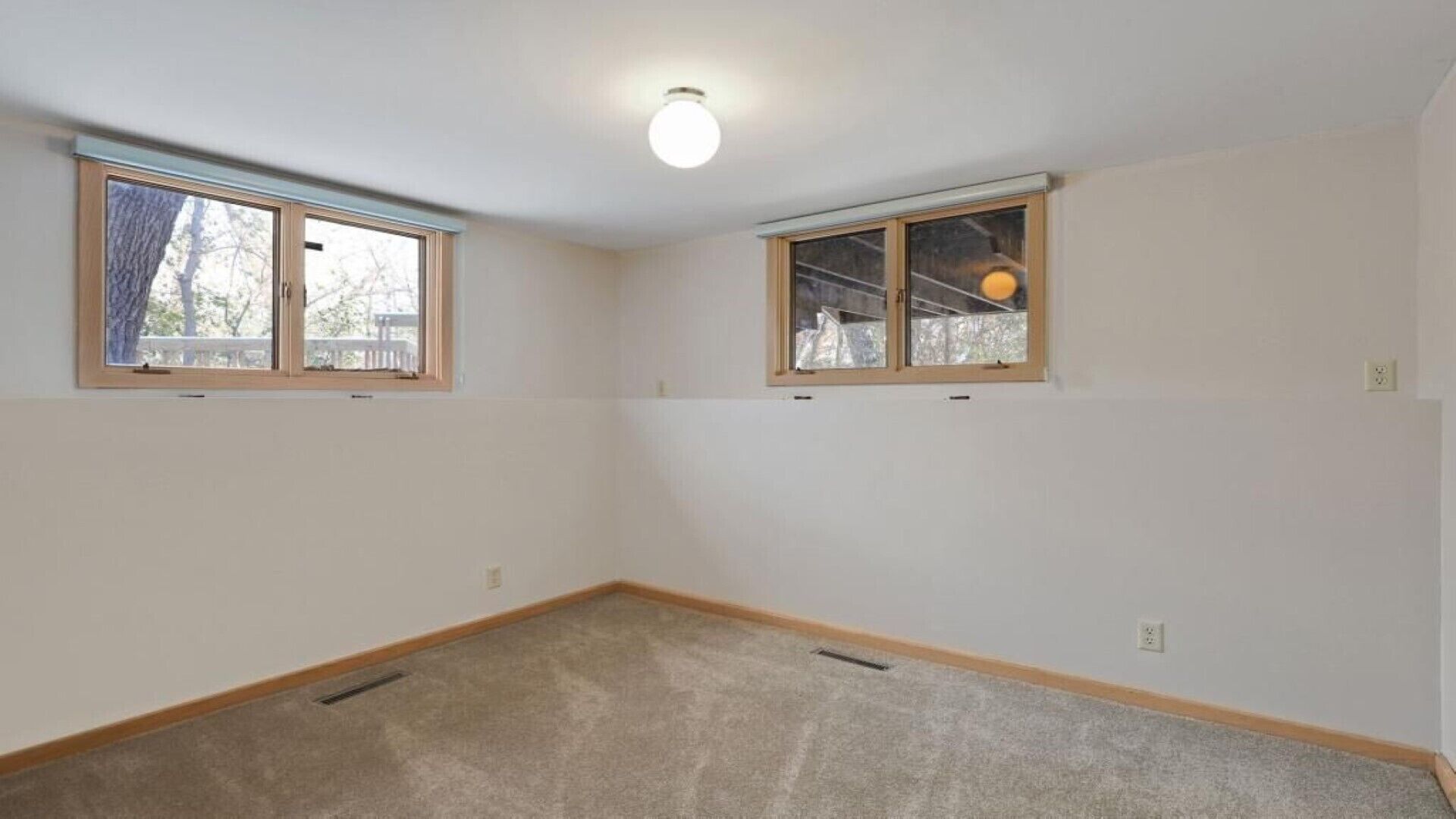A room with two windows, a ceiling light, and carpeted flooring.