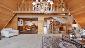 Un loft spacieux avec de hauts plafonds, des poutres apparentes, un lustre, un coin repas et un escalier.