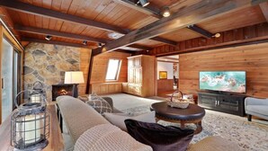 Un salon chaleureux avec une cheminée en pierre, des poutres en bois, un téléviseur et des sièges confortables.