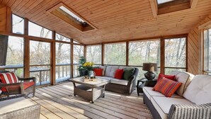 Une véranda avec de grandes fenêtres, des meubles en osier et une terrasse en bois.