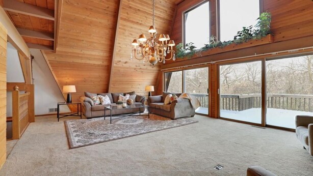 Un vaste salon doté d’un haut plafond, d’un lustre, d’une grande fenêtre offrant une vue sur un paysage enneigé et d’un escalier en bois.