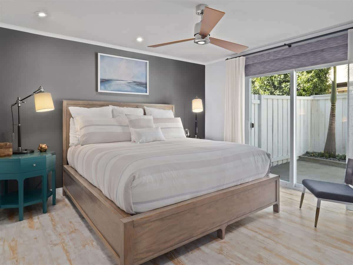 A bedroom with a bed, bedside lamps, a ceiling fan, and a view through a sliding glass door.