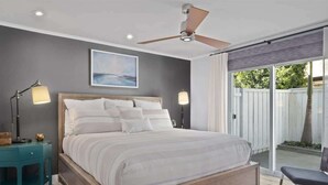 A bedroom with a bed, bedside lamps, a ceiling fan, and a view through a sliding glass door.