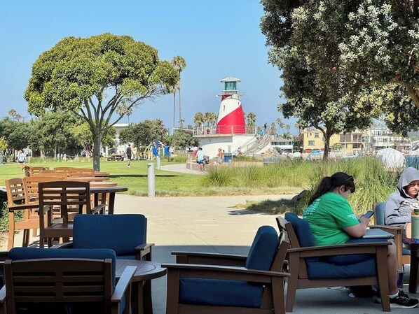 Un espace extérieur aménagé avec des tables et des chaises, un phare en arrière-plan et un ciel dégagé.