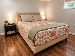 A bedroom with a bed, nightstands, a lamp, a small plant, and a window.